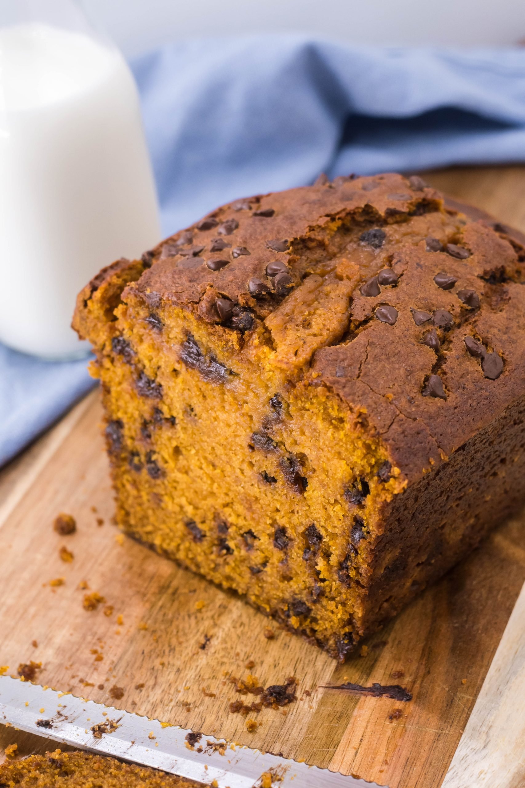 a loaf of crockpot pumpkin bread sliced open and shown on a cutting boar with fresh milk in the background