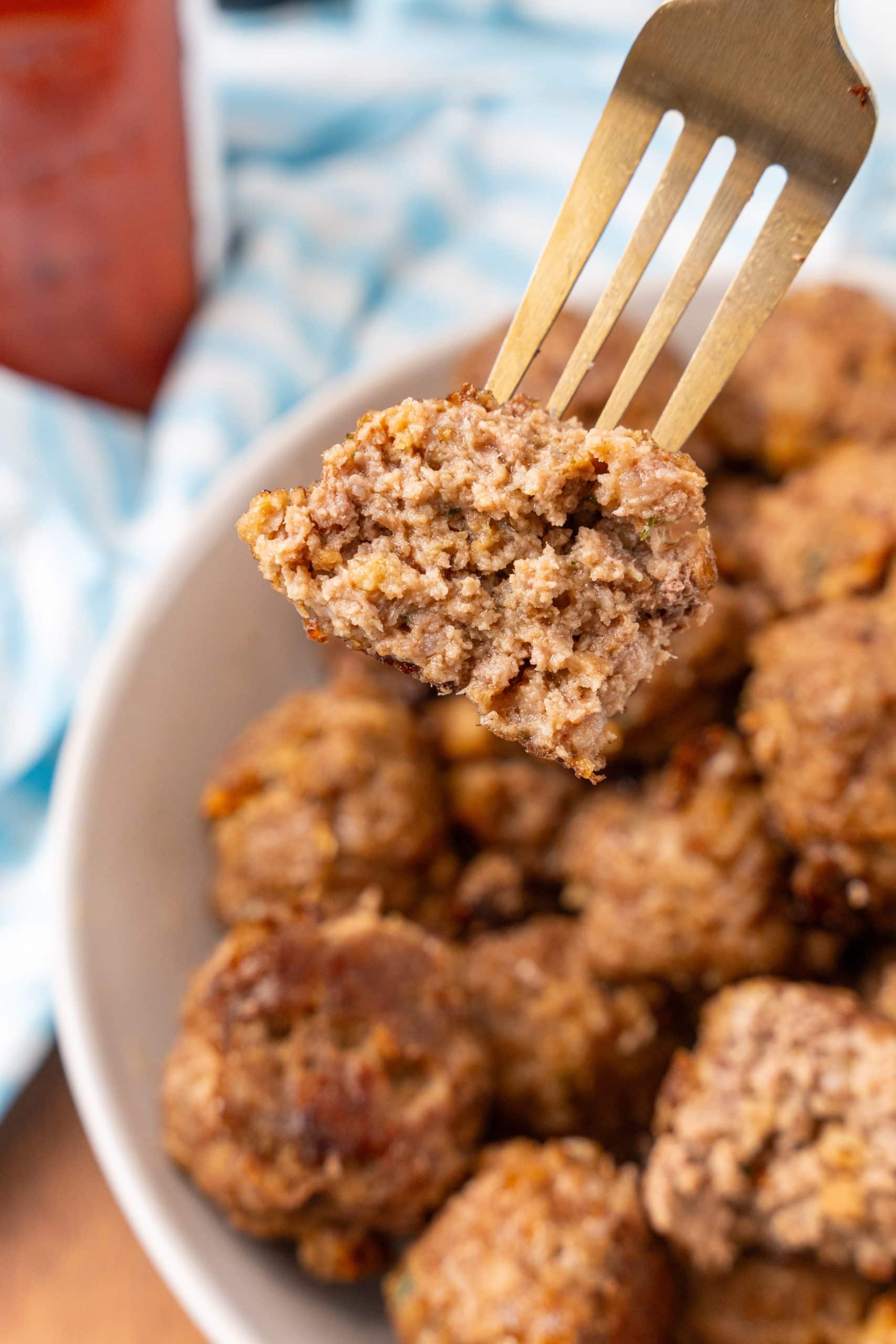 a golden fork holding up half of a crispy baked beef meatball
