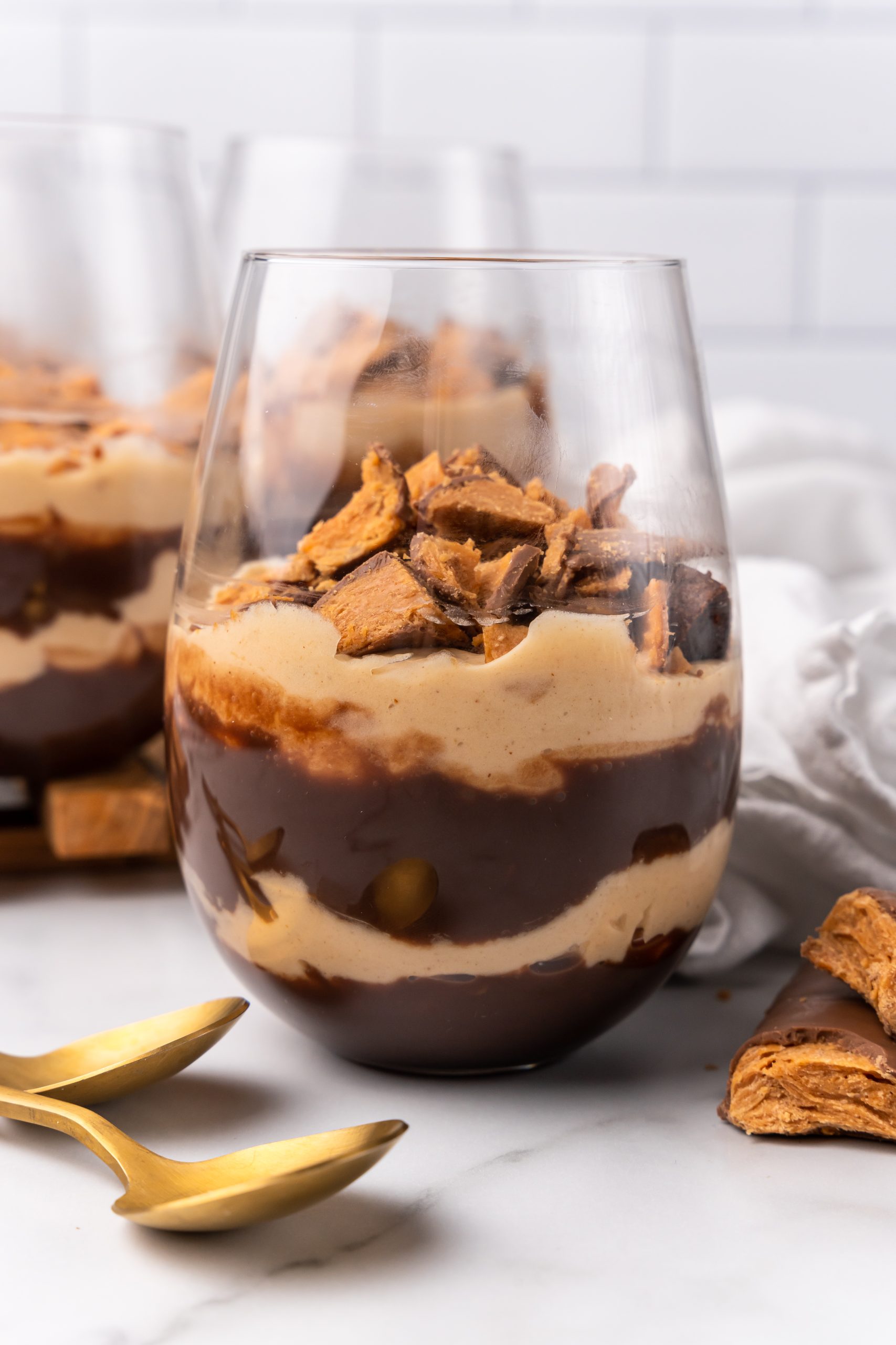 a layered butterfinger trifle on a stemless wine glass on a wooden cutting board
