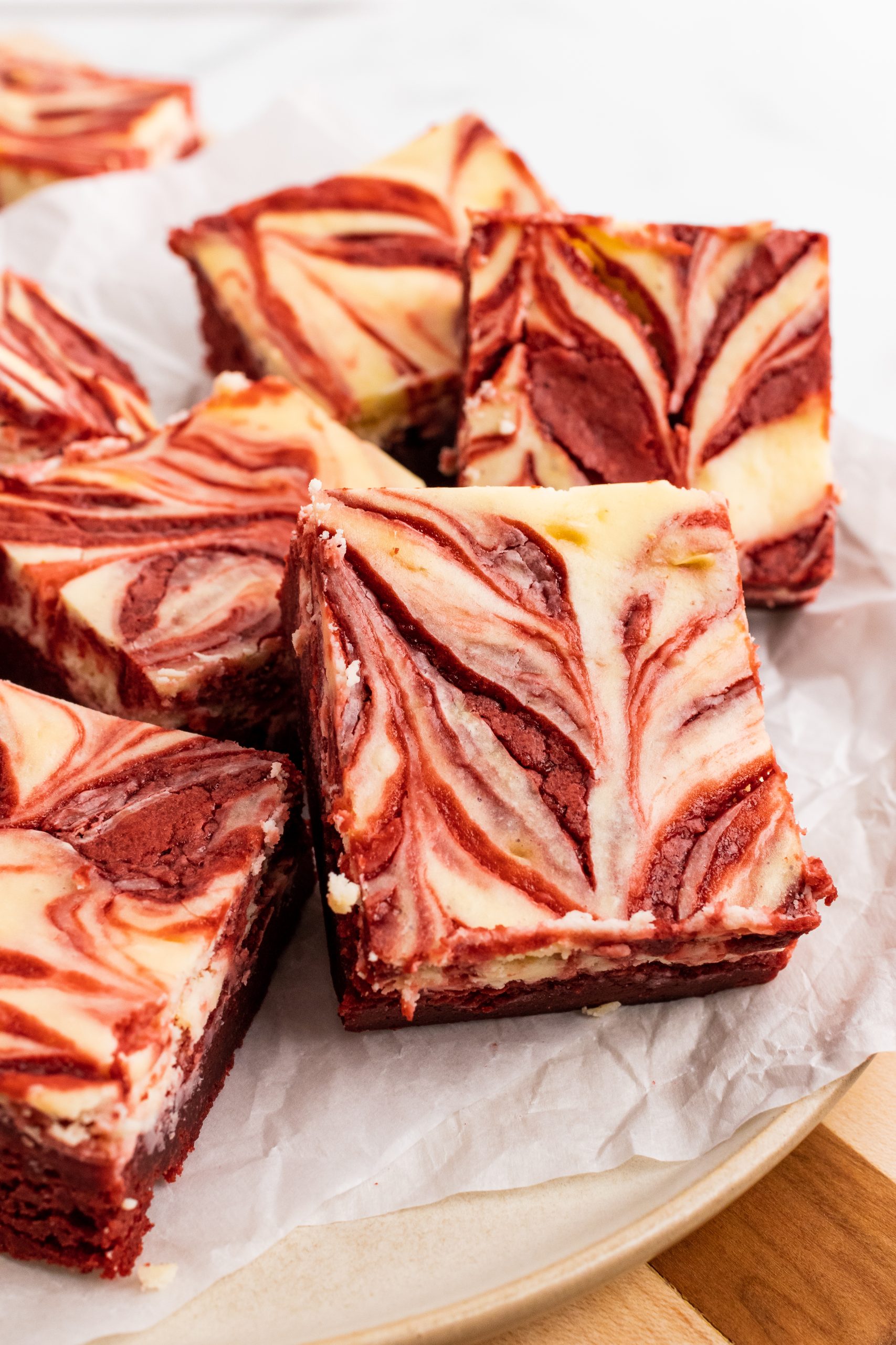 red velvet cheesecake brownie squares in a pile on a parchment paper covered cutting board