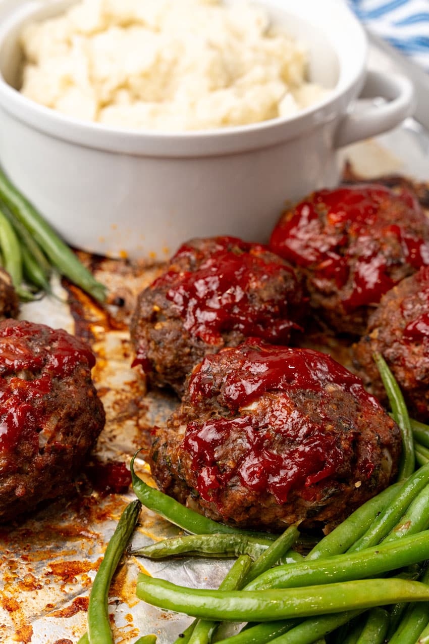roasted green beans, mini meatloaves, and a bowl of mashed potatoes on a metal sheet pan