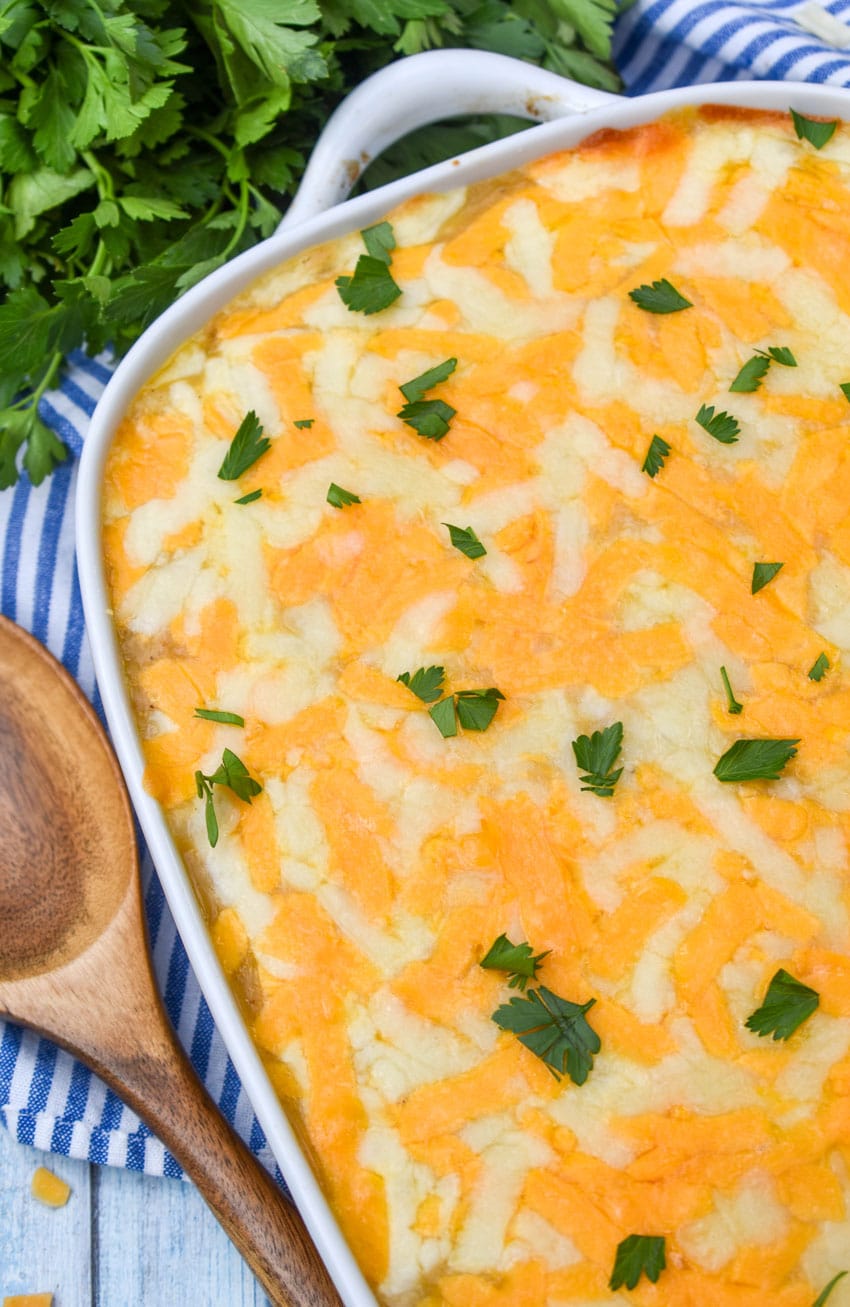 chicken rice pilaf casserole topped with fresh herbs in a white baking dish with a wooden spoon on the side