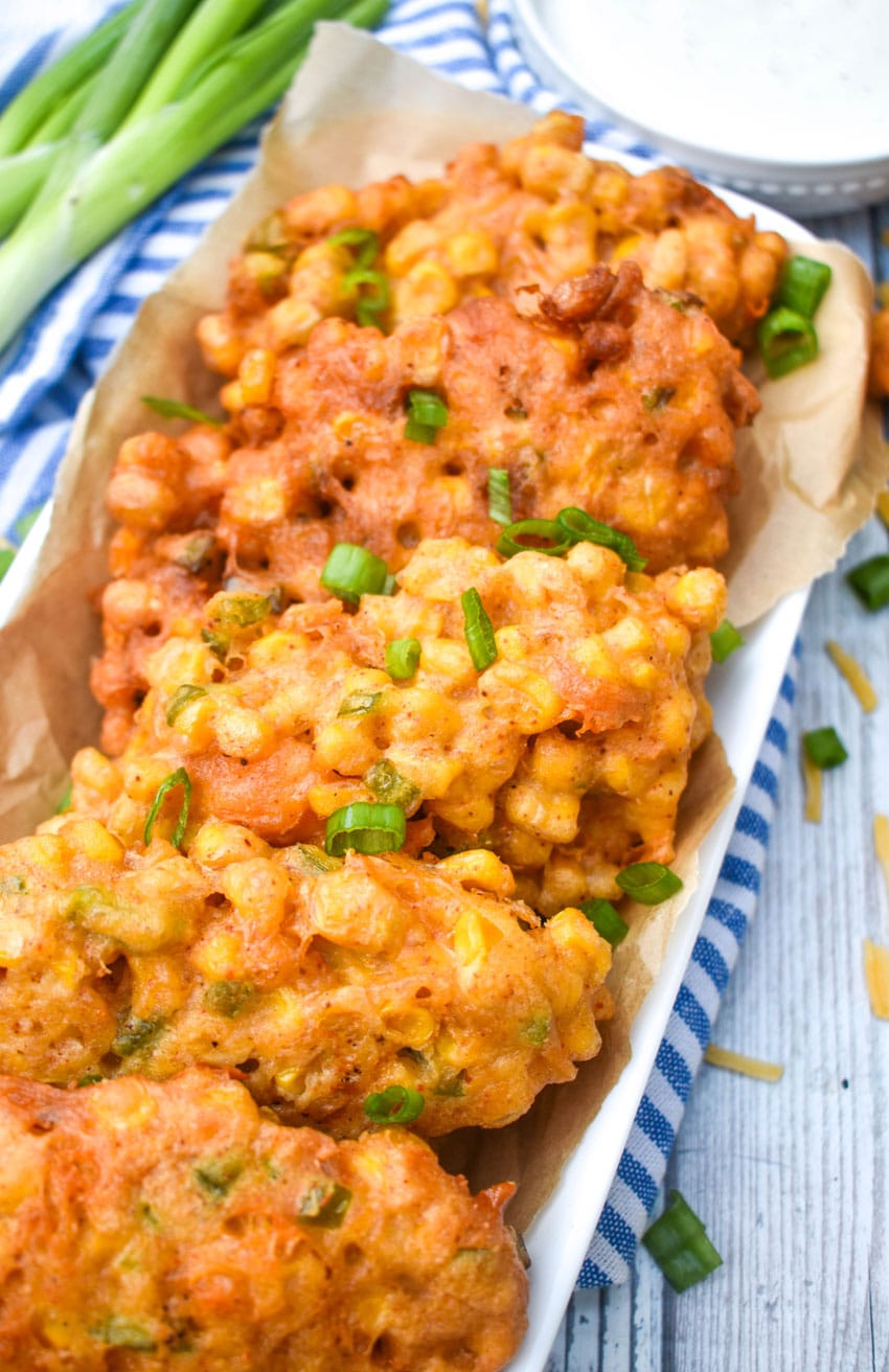sweet corn and cheddar cheese fritters on a brown parchment paper lined white serving platter