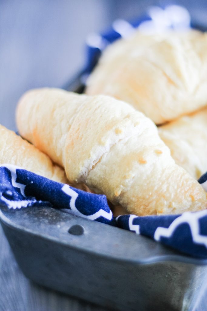 a pile of flaky, baked homemade crescent rolls in a cloth napkin lined metal loaf pan