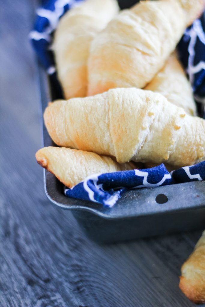 a pile of flaky, baked homemade crescent rolls in a cloth napkin lined metal loaf pan