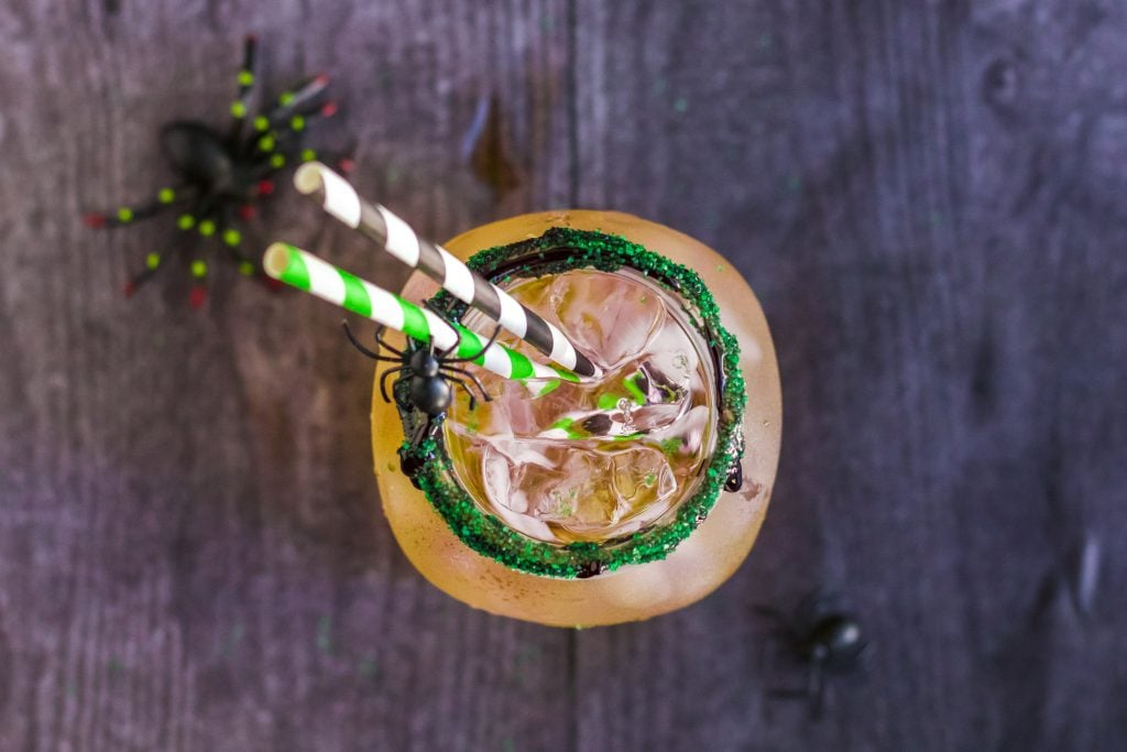 green, orange, and purple Halloween themed layered drink with ice in a glass mason jar rimmed with black icing and edible glitter