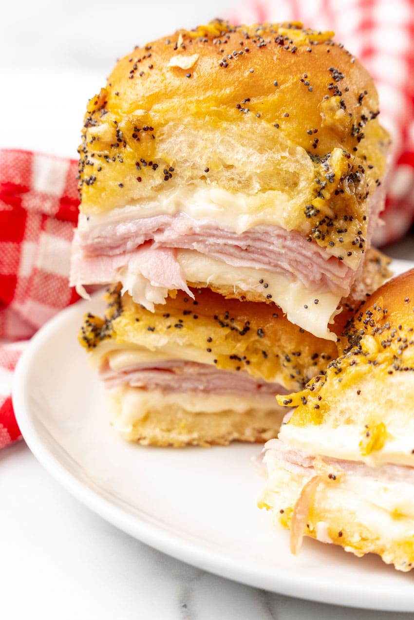 two hot ham and cheese sliders stacked together resting on a small white plate