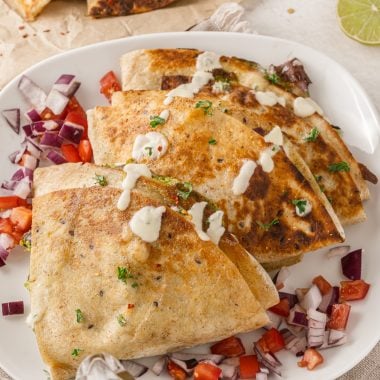 tiktok folded quesadillas stacked on a white plate, topped with tomatoes, red onions, cilantro, and drizzled with sour cream