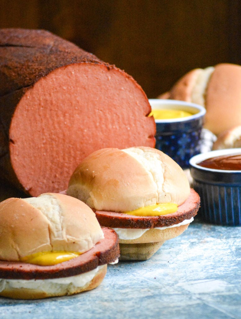 smoked bologna sandwiches served in front of the smoked bologna chub on a wooden cutting board