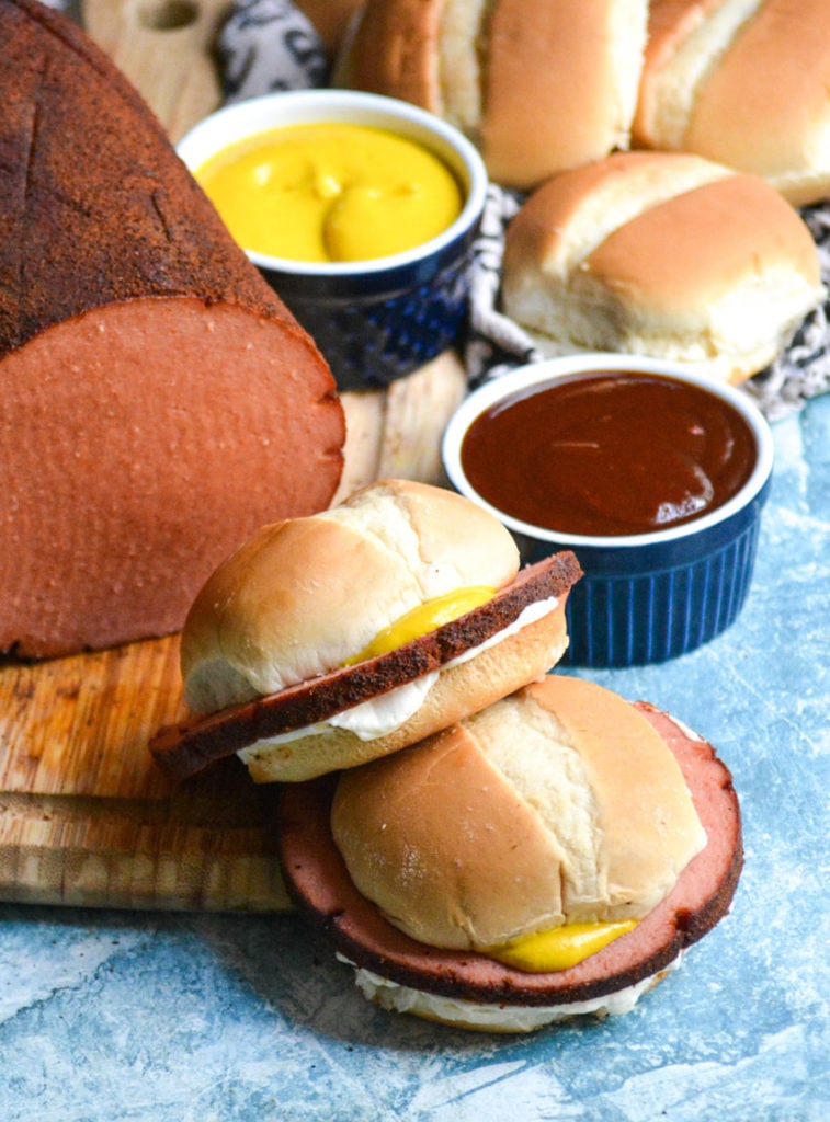 smoked bologna sandwiches served in front of the smoked bologna chub on a wooden cutting board