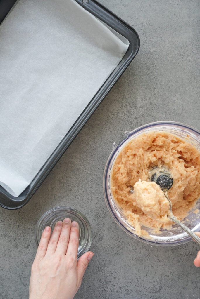 a hand dipped in a bowl of water next to a spoonful of seasoned ground chicken