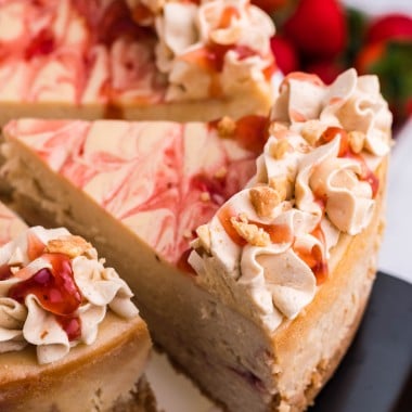 a silver spatula removing a slice of peanut butter & jelly cheesecake from a white cake stand