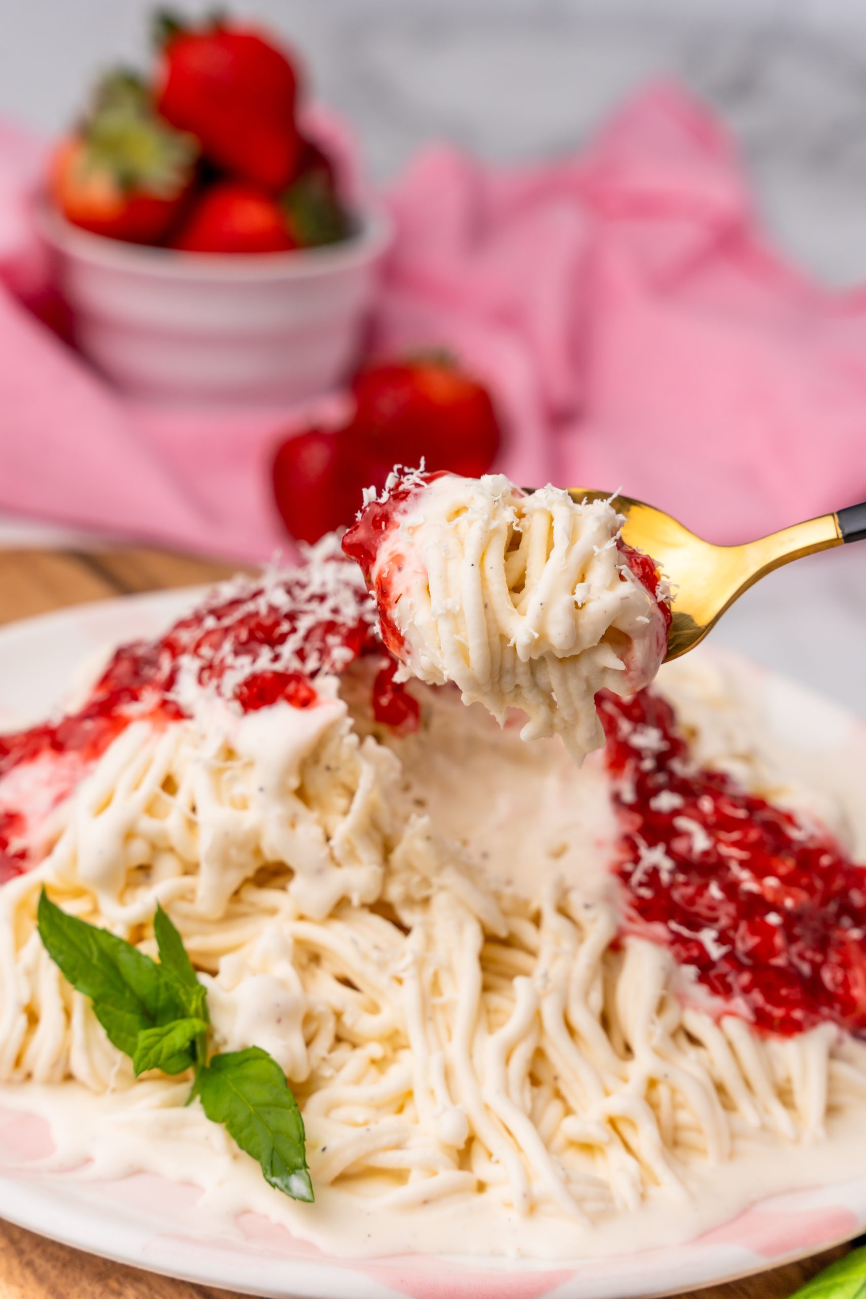 a gold spoon holding up a scoop of strawberry topped spaghetti eis ice cream noodles