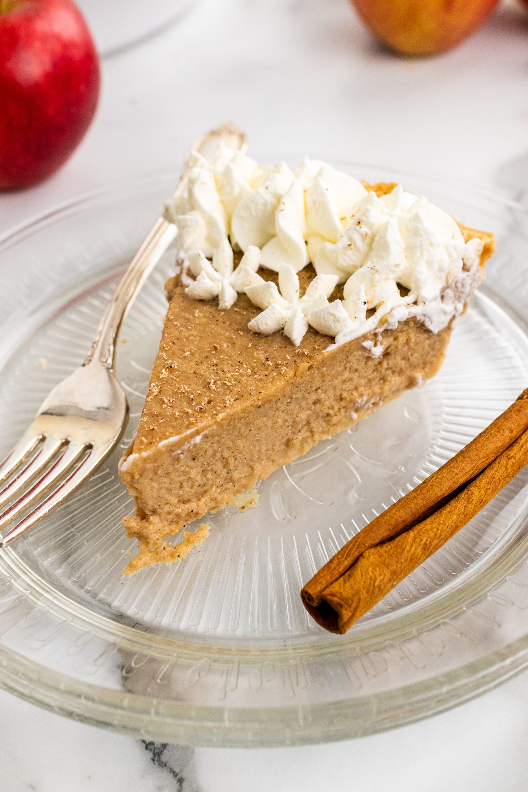 a slice of apple butter pie on a glass plate with a cinnamon stick on the side