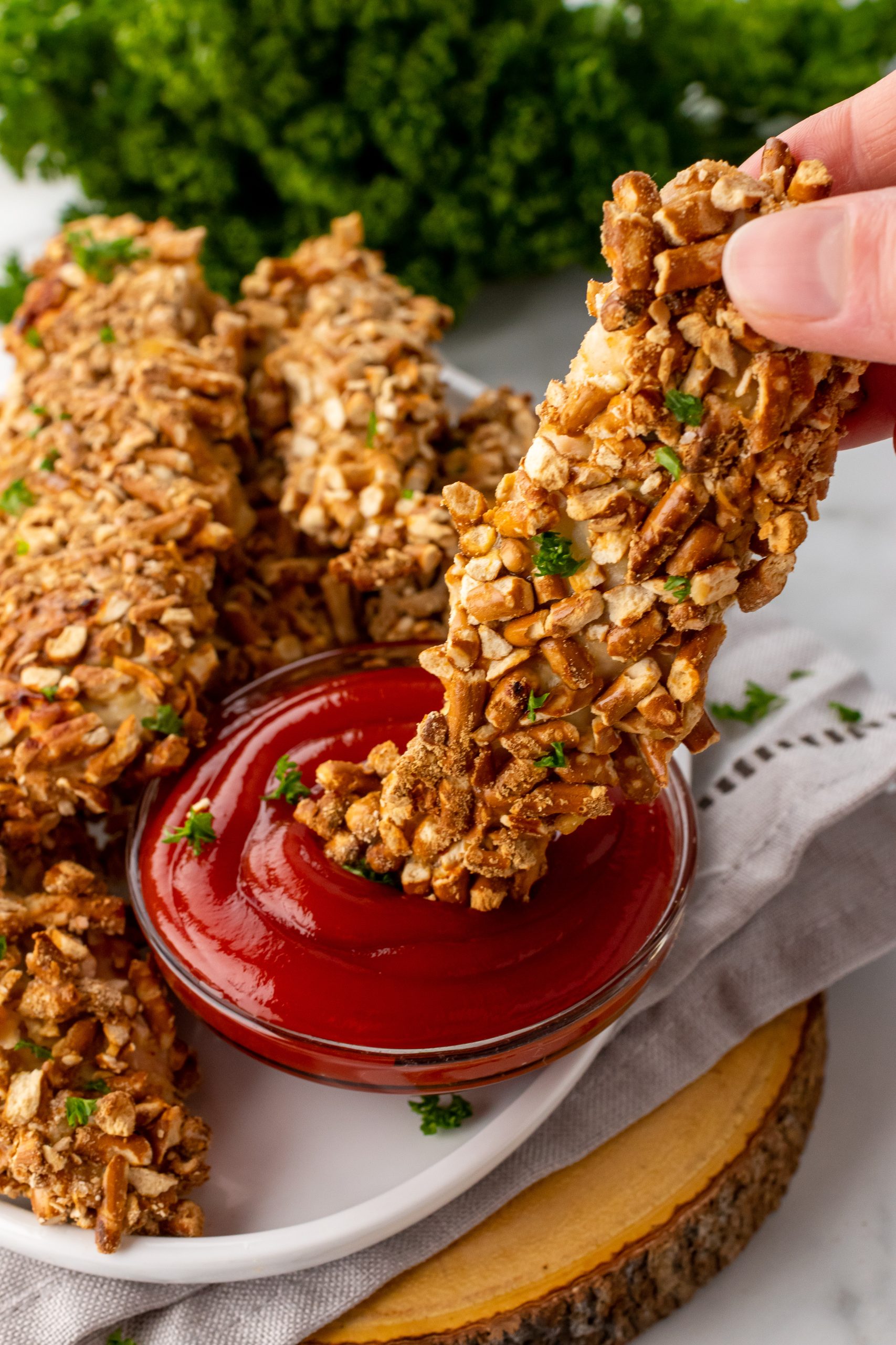 a hand dunking a pretzel chicken tender in a small glass bowl filled with ketchup