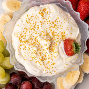 a strawberry in a golden sprinkle topped bowl of champagne cheesecake fruit dip