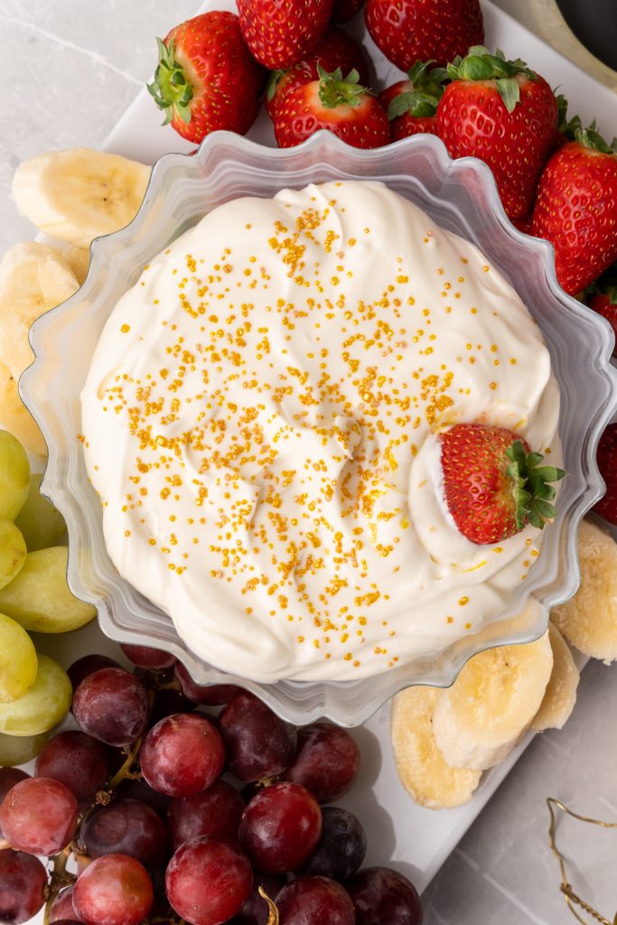 a strawberry in a golden sprinkle topped bowl of champagne cheesecake fruit dip