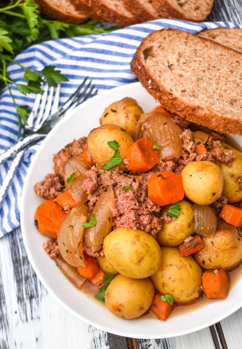 slow cooker corned beef hash in a white bowl with a slice of crusty bread on the side