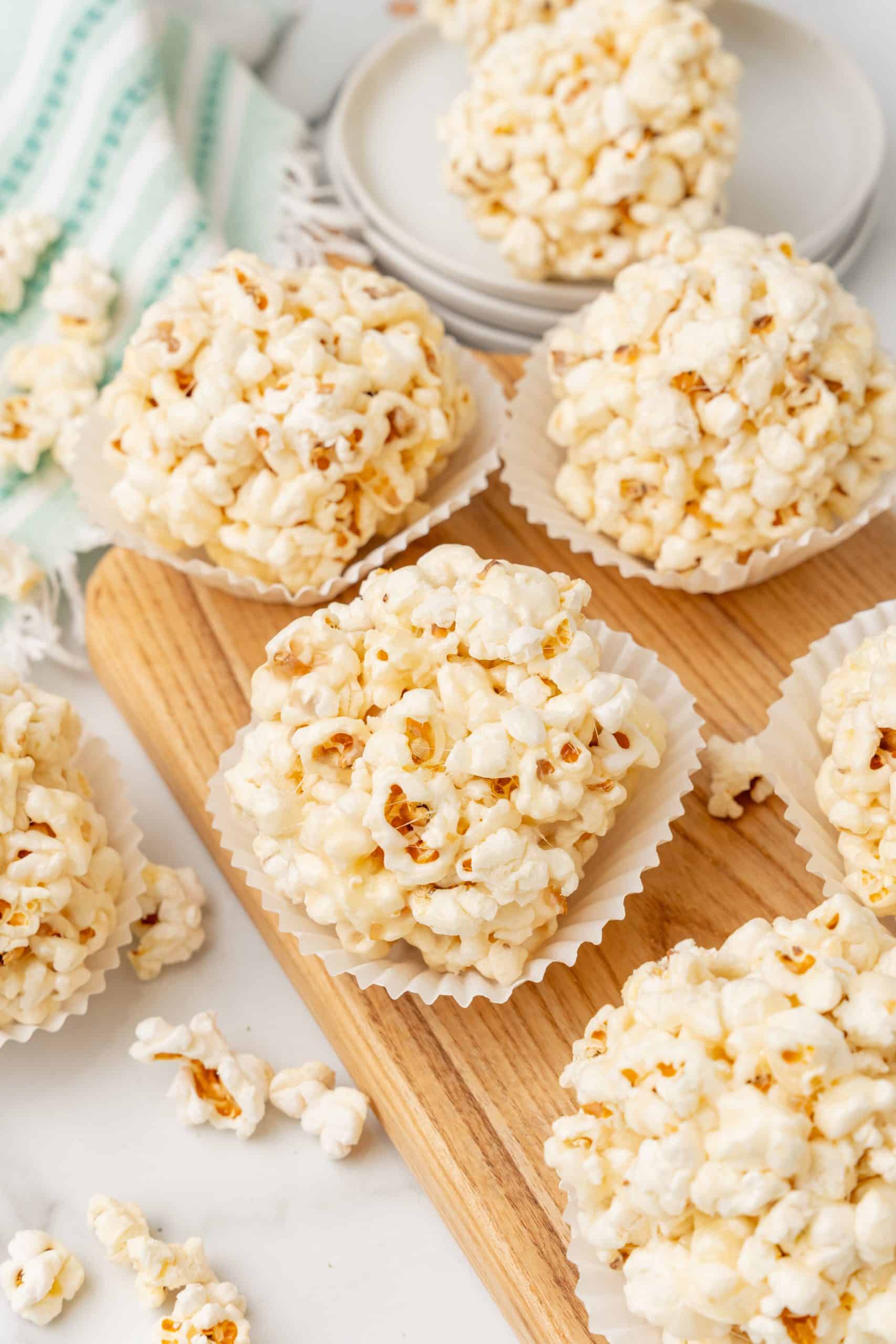 marshmallow popcorn balls in white cupcake liners on a wooden cutting board