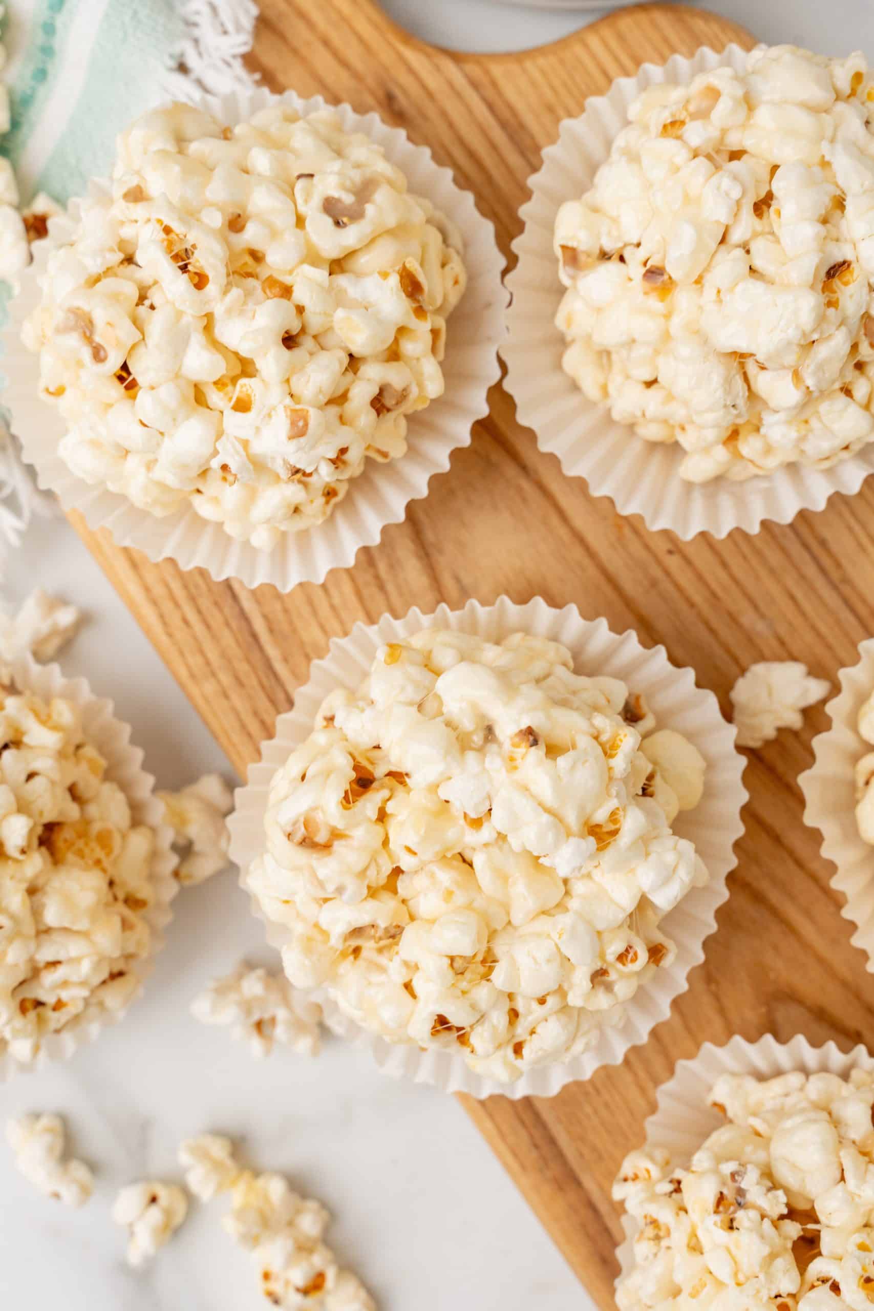 marshmallow popcorn balls in white cupcake liners on a wooden cutting board