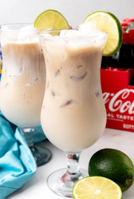 two dirty sodas over ice in daquiri style glasses with a slice of lime on the rim