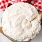 a bowl full of homemade cool whip with a golden serving spoon resting on the side