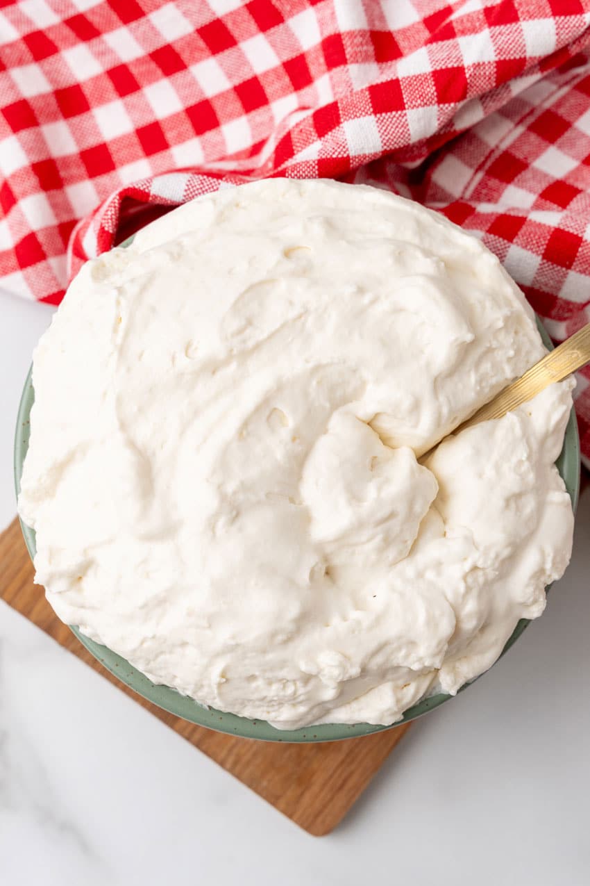 a bowl full of homemade cool whip with a golden serving spoon resting on the side